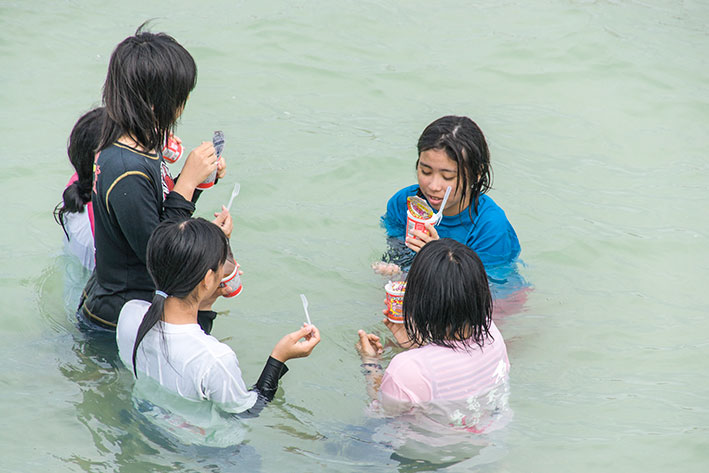 ５月４日のスナップ。奥武島の海でブタメンを食べる女子